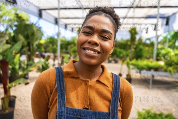 Portrait of a young african american woman working in a greenhouse, smiling confidently amidst lush greenery