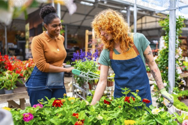 Two young women working in a garden center taking care of colorful flowers and helping customers