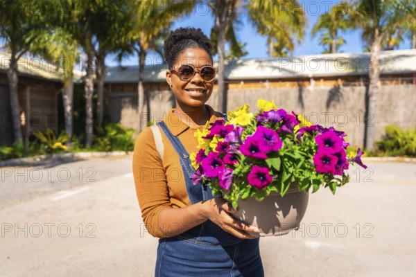 Smiling gardener holding a large pot filled with vibrant, colorful flowers, surrounded by a sunny tropical resort setting