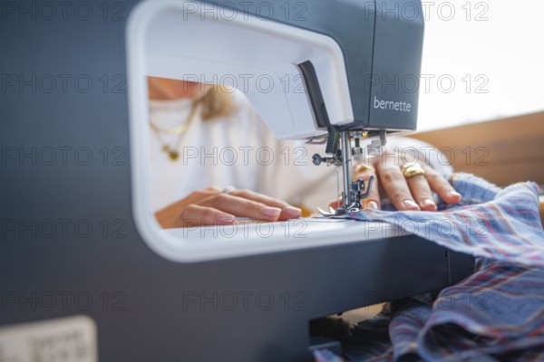 Sewing a chequered fabric with a sewing machine, hands guide the fabric under the needle