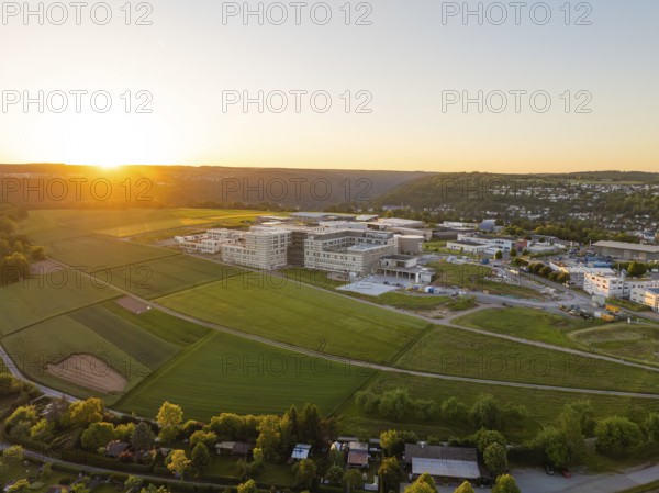 View of fields and a large building in a hilly landscape at sunset, Calw, Black Forest, Germany