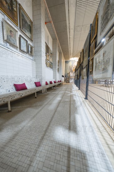 A long corridor in an art gallery with numerous paintings on the walls and a white bench with red cushions, historical art exhibition in the old swimming pool, Schaudepot, Calw, Black Forest, Germany
