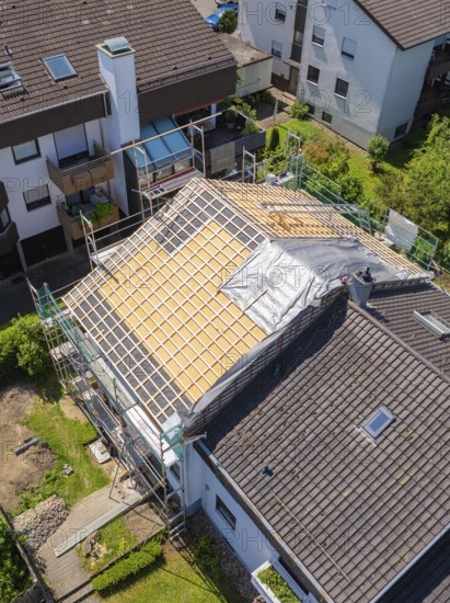 House with scaffolding and part of the roof covered, in a sunny residential area, roof renovation, house construction, Pforzheim, Germany