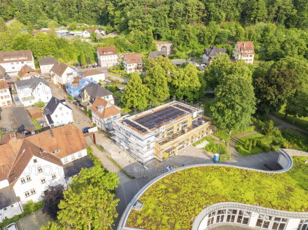View of a residential area with a building site in the centre and green areas on some roofs, surrounded by trees, Hirsau, Calw, Germany
