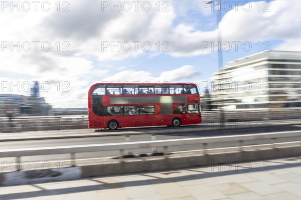 Red double decker bus driving across london bridge, capturing the essence of london's vibrant transportation