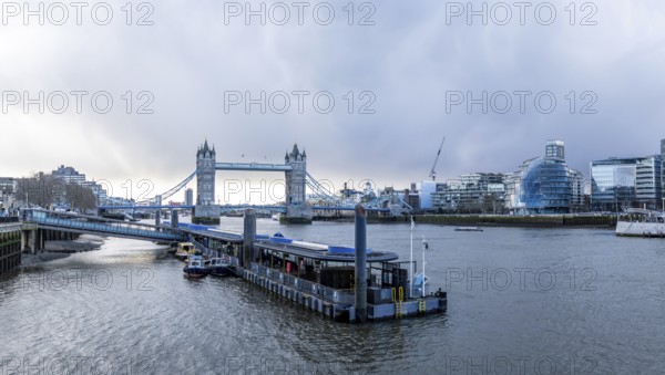 Tower bridge rising above river thames with city hall and modern buildings in background, capturing essence of london's cityscape on overcast day