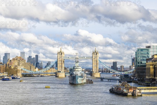 Hms belfast, a town class light cruiser, sailing on the river thames with tower bridge and cloudy sky in the background