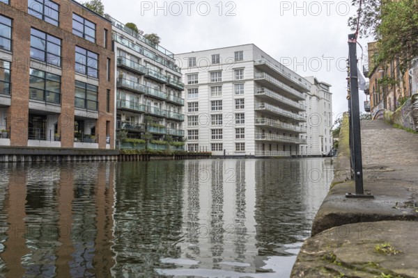 Modern and historic buildings reflecting in the calm waters of regent's canal in the city of london on a cloudy day
