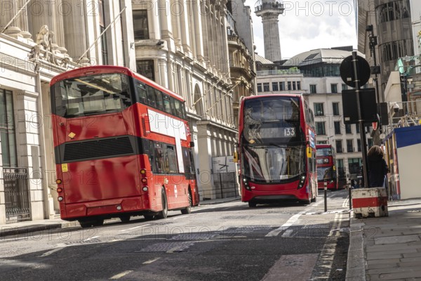 Red double decker buses driving on a street in the city of london, passing by classical buildings