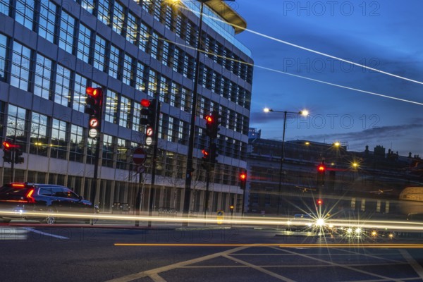 Cars passing by on a london street at dusk, with traffic lights turning red and offices in the background