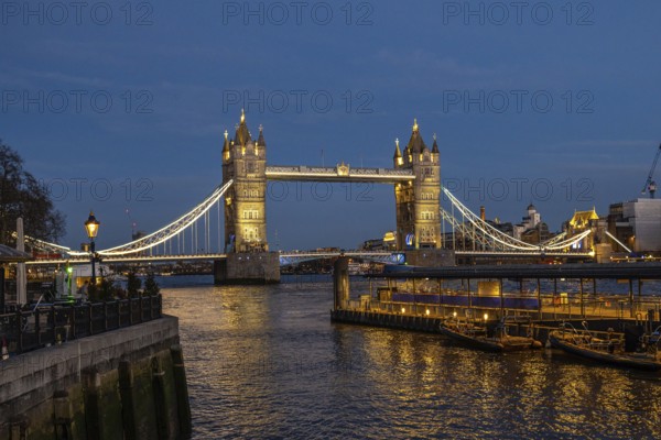 Tower bridge stands majestically illuminated against the twilight sky, its lights reflecting on the river thames
