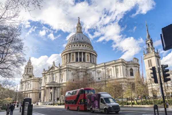 Red double decker bus driving on a street next to st paul's cathedral in london, uk, on a sunny spring day