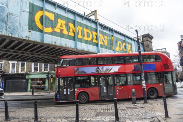 Iconic red double decker bus driving through camden town in london, under the bridge with the camden lock writing