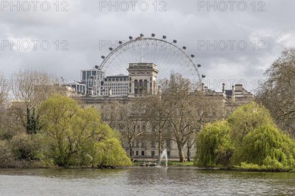 Scenic view of the london eye ferris wheel rising above st. James's park, featuring a tranquil lake, fountain, and lush trees, capturing the essence of london's cityscape and natural beauty