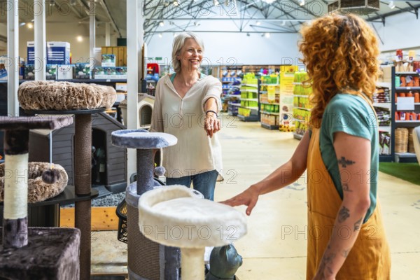 Senior woman buying a cat tree in a pet shop, helped by a young sales assistant, choosing the right product for her needs