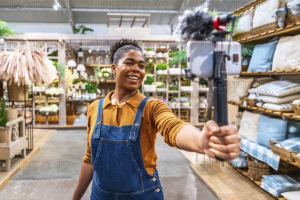 Smiling influencer recording video content with smartphone and microphone for social media marketing campaign in a home decor store