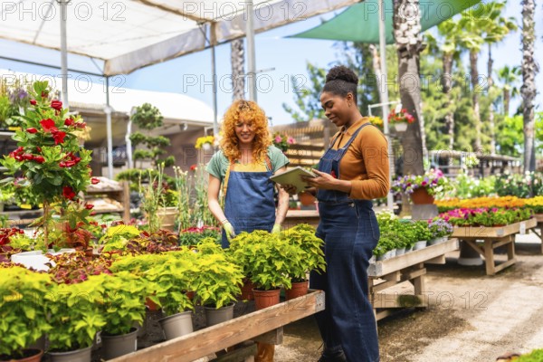 Two women collaborating in a garden center, consulting a digital tablet while discussing various plants and their care
