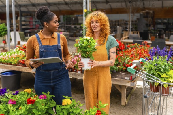 Two young women working in a garden center, discussing plants and using a digital tablet for inventory or customer assistance