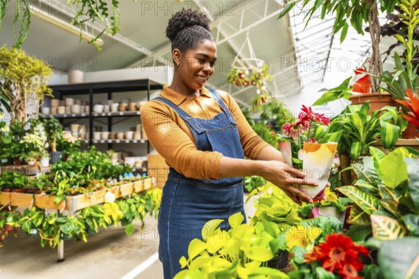 Smiling young woman working in a plant shop arranging potted flowers and houseplants on display