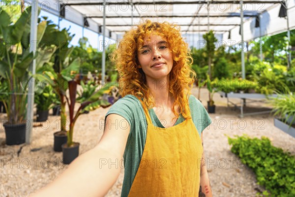Confident red haired female gardener taking a selfie in a greenhouse, showcasing her passion for plants and sustainable living