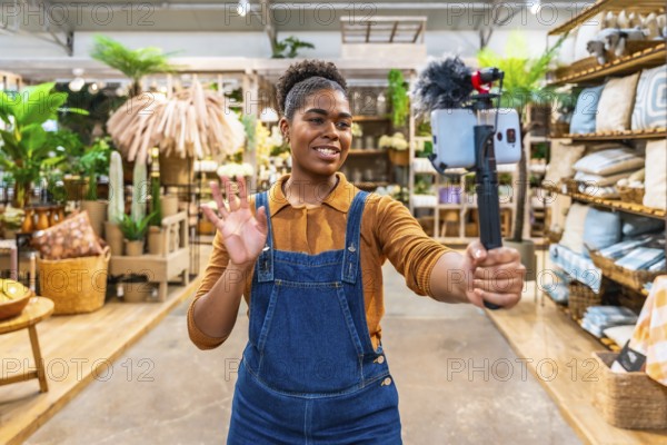 Young saleswoman waving and streaming live video using a smartphone and microphone inside a furniture store