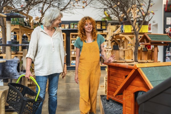 Smiling saleswoman showing wooden dog houses to customer carrying shopping basket in a pet shop