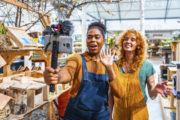 Two happy saleswomen waving at the camera while filming a video for social media marketing in a pet shop