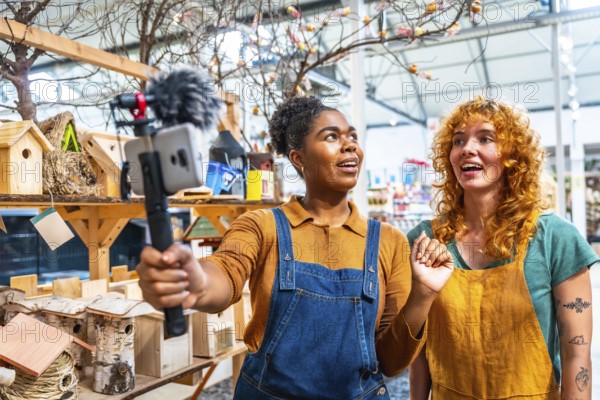 Two young women working in a garden center filming a video for social media using a smartphone with external microphone
