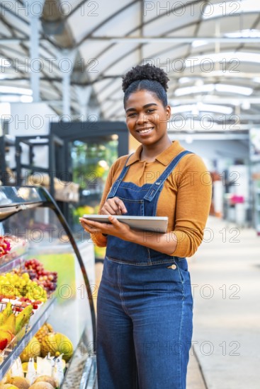 Young supermarket employee managing fresh fruit section inventory using a digital tablet, ensuring quality and availability for customers