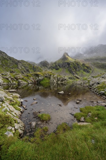 Small mountain lake, cloudy mountain peaks reflected in the lake, Schober group, Hohe Tauern National Park, Carinthia, Austria