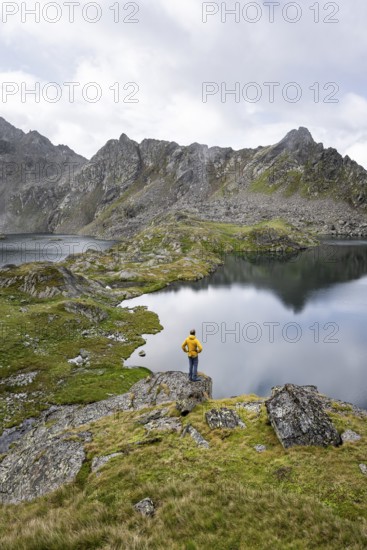 Mountaineer on a rock in front of mountain lakes Wangenitzsee and Kreuzsee, cloudy mountain peaks in the morning, Schober group, Hohe Tauern National Park, Carinthia, Austria