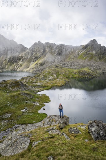 Mountaineer on a rock in front of mountain lakes Wangenitzsee and Kreuzsee, cloudy mountain peaks in the morning, Schober group, Hohe Tauern National Park, Carinthia, Austria