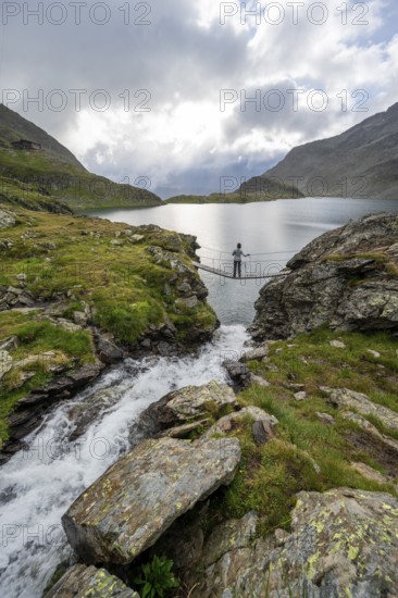 Mountaineer standing on a suspension bridge, mountain stream and mountain lake Wangenitzsee, Schober Group, Hohe Tauern National Park, Carinthia, Austria