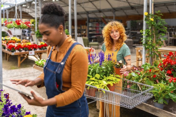 Two young women working in a garden center, taking care of plants and using a digital tablet for inventory management