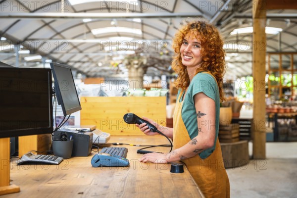 Young saleswoman holding barcode scanner, ready to scan products at checkout counter in modern garden center