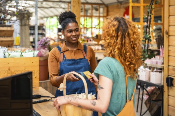 Friendly shop assistant holding credit card reader while customer making contactless payment in a flower shop