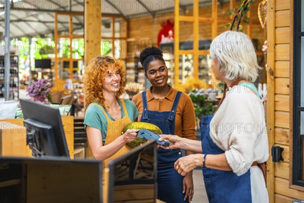 Customer paying with contactless payment in a grocery store, assisted by two smiling shop assistants