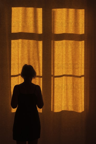 Back view of a woman standing in front of a window with a red curtain