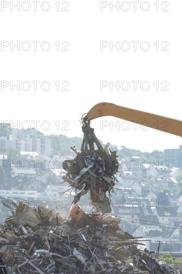 Hydraulic crane lifts scrap metal at the scrapyard in the background a city
