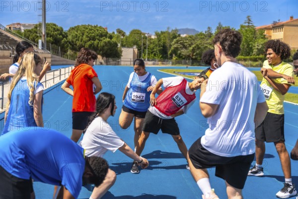 Teenage athletes stretching their legs and arms on a vibrant blue track, engaging in warm up exercises before an upcoming competition