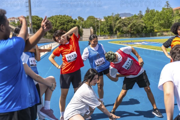 Teenagers wearing bib numbers stretching together on a blue running track before a track and field competition