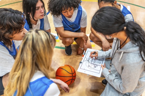 Female basketball coach drawing a play on a whiteboard and explaining game strategy to her young multi ethnic team during a time out