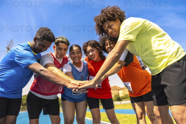Diverse group of athletes gathers on a running track, joining hands in a circle, symbolizing teamwork, unity, and sportsmanship