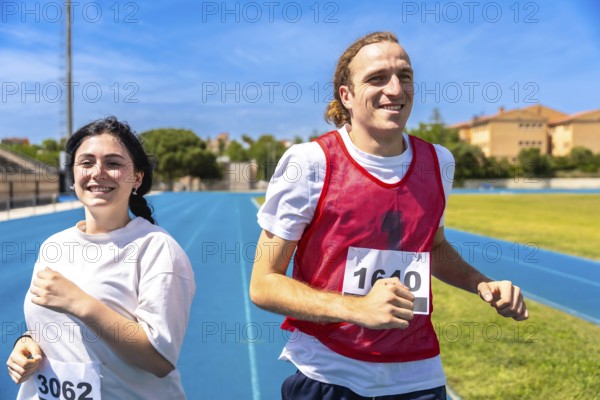 Two happy athletes running a race on a blue track at an athletics stadium under a clear blue sky