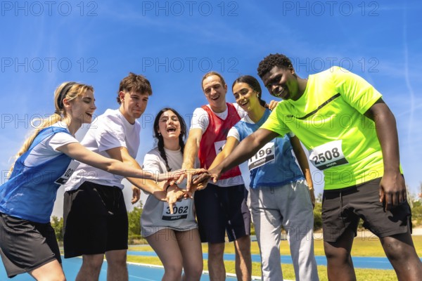 Diverse group of young athletes putting their hands together before a track and field competition, showing teamwork and sportsmanship