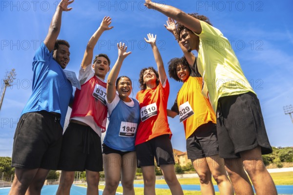 Group of young runners celebrating their victory with arms raised high after crossing the finish line on a vibrant running track