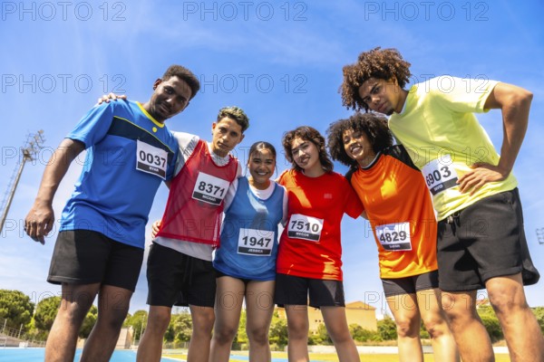 Diverse group of athletes embracing teamwork and camaraderie on a running track, celebrating sportsmanship and athletic achievement