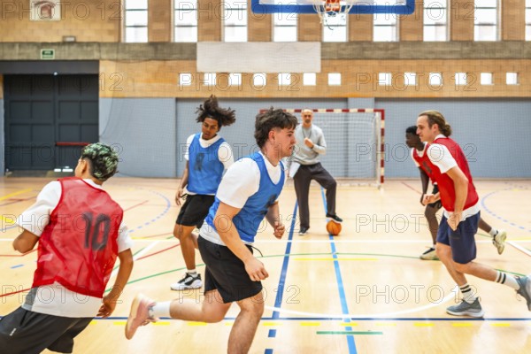 Group of young basketball players running on court during training session with coach watching and ball on floor