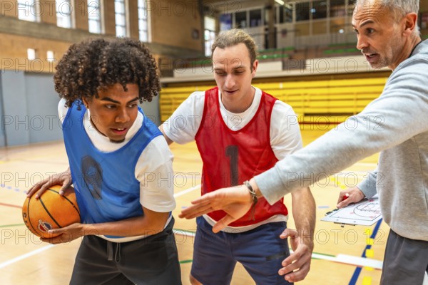 Basketball coach explaining game strategy using clipboard to two players wearing training bibs