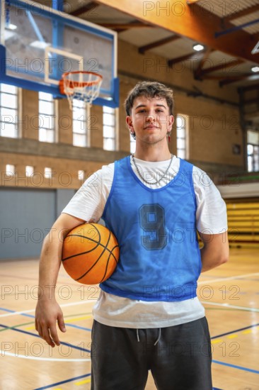 Young male basketball player holding ball in indoor court posing after training, looking confident and ready for the next game